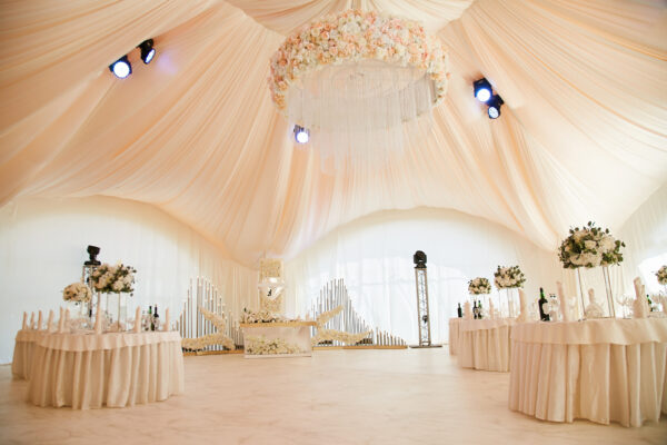 Wedding ceremony in a beautiful tent. Hall with dining tables decorated with bouquets of flowers.