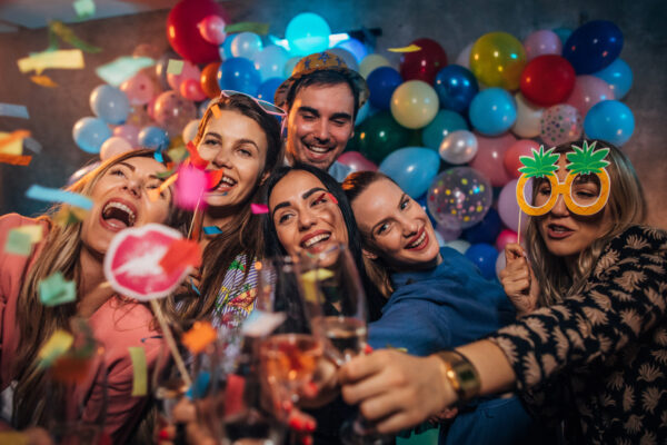 Group of young women and men having fun with balloons and photo booth at a party