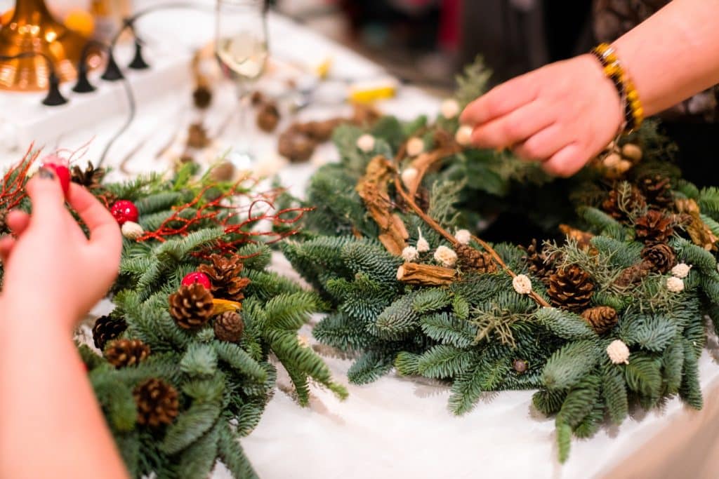 Hands crafting Christmas wreath with pine cones and berries