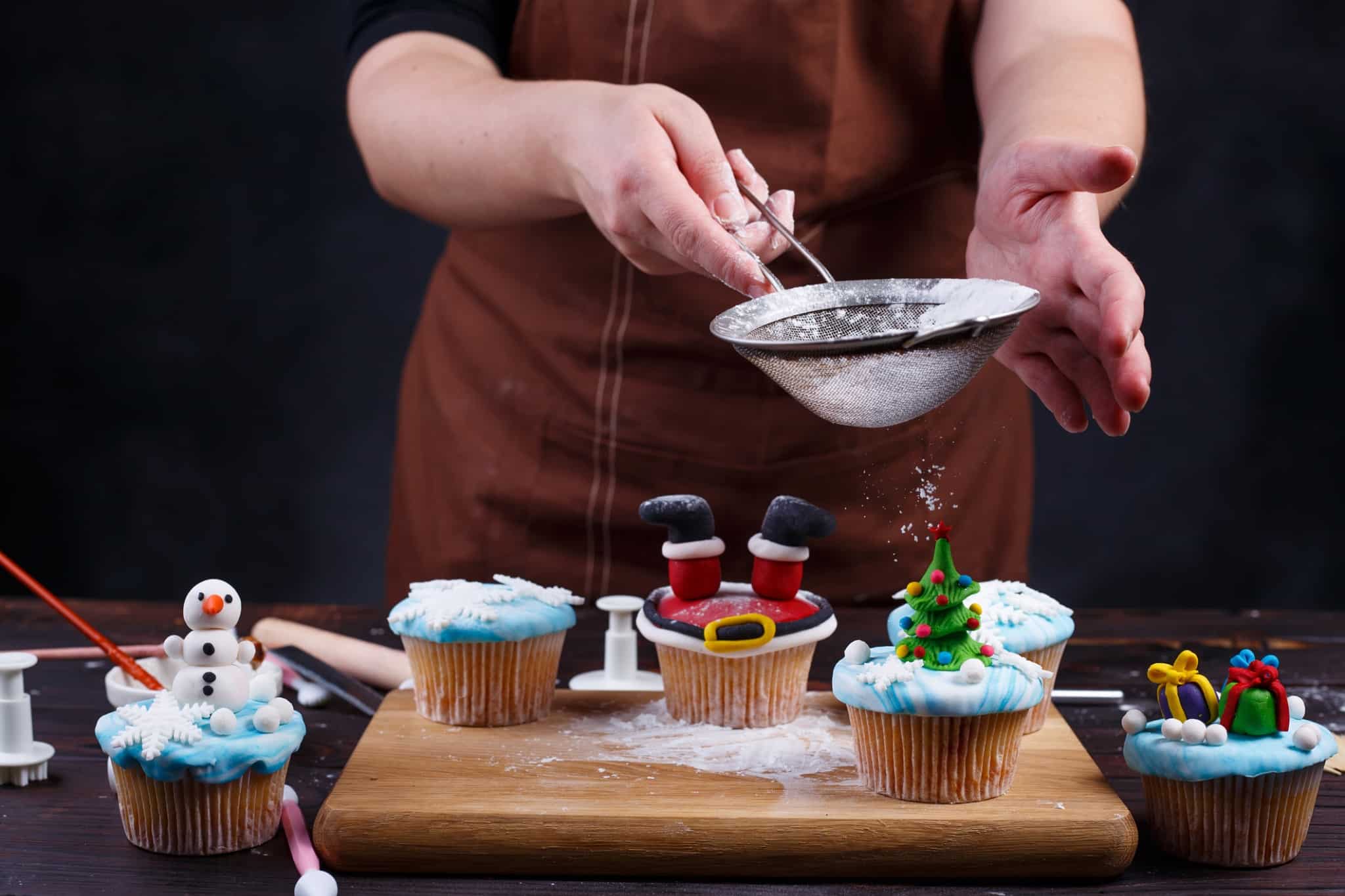Person decorating festive cupcakes with Christmas designs