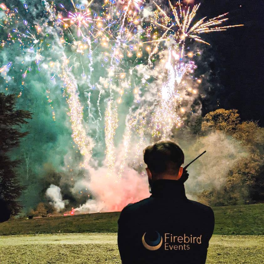 Firebird Events technician overseeing a large professional fireworks display with a walkie-talkie.