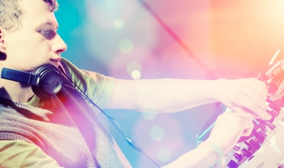 Event DJ with headphones mixing music on a brightly lit console at a party or festival.