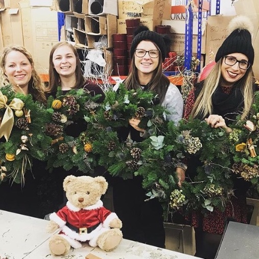 Women holding festive Christmas wreaths with a teddy bear decoration in front