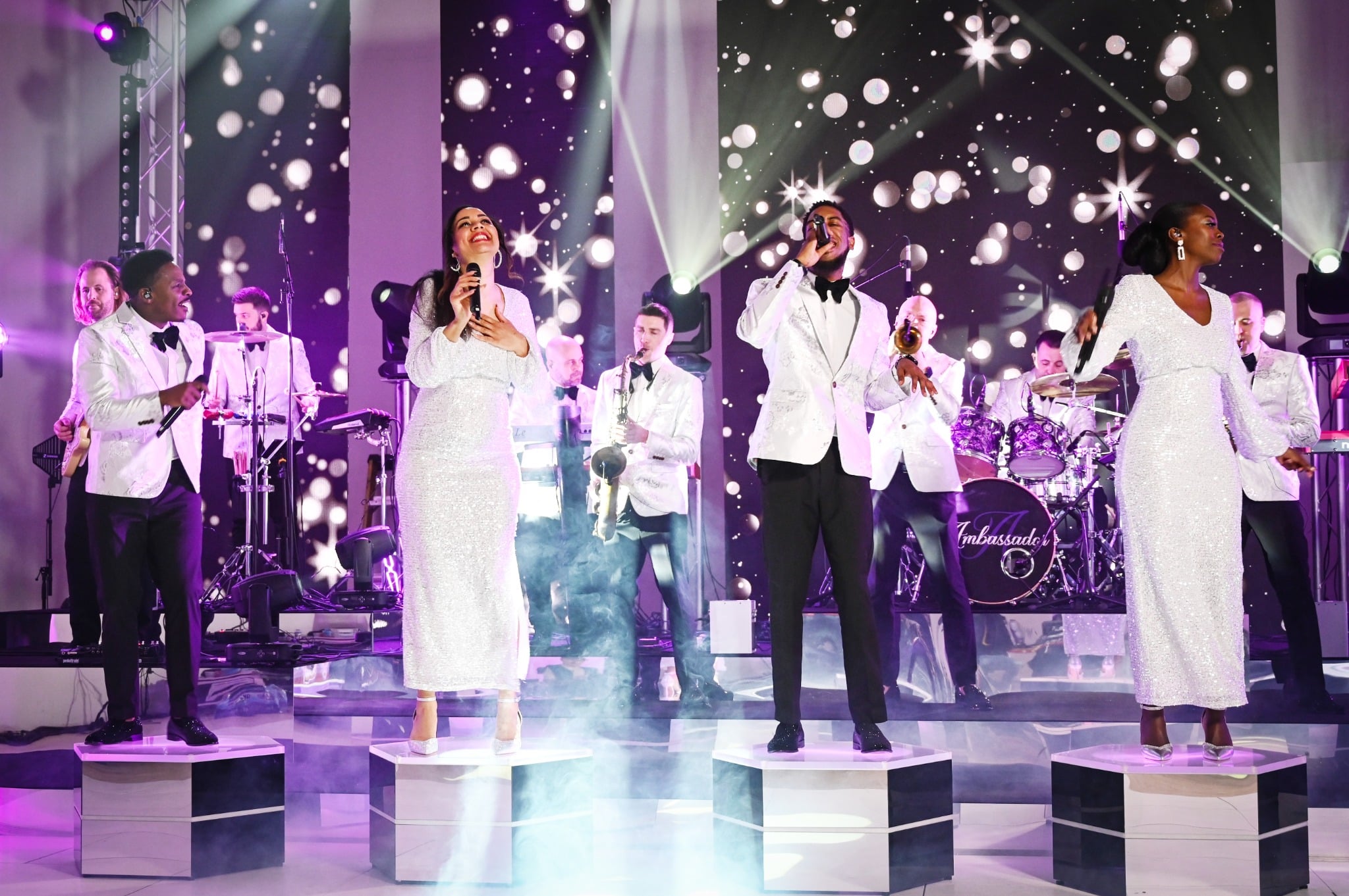 Live band performing on stage in elegant white outfits with singers and musicians under dramatic event lighting