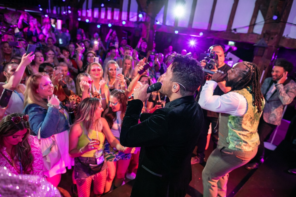 Male singer performing on stage with a lively audience dancing and recording on their phones