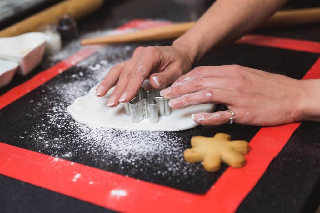 Hands cutting festive Christmas cookies with a cutter.