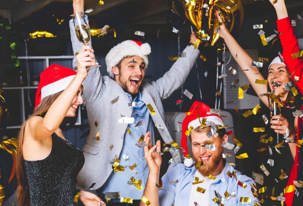 Colleagues celebrating at a festive Christmas party with Santa hats, drinks and confetti during a corporate event